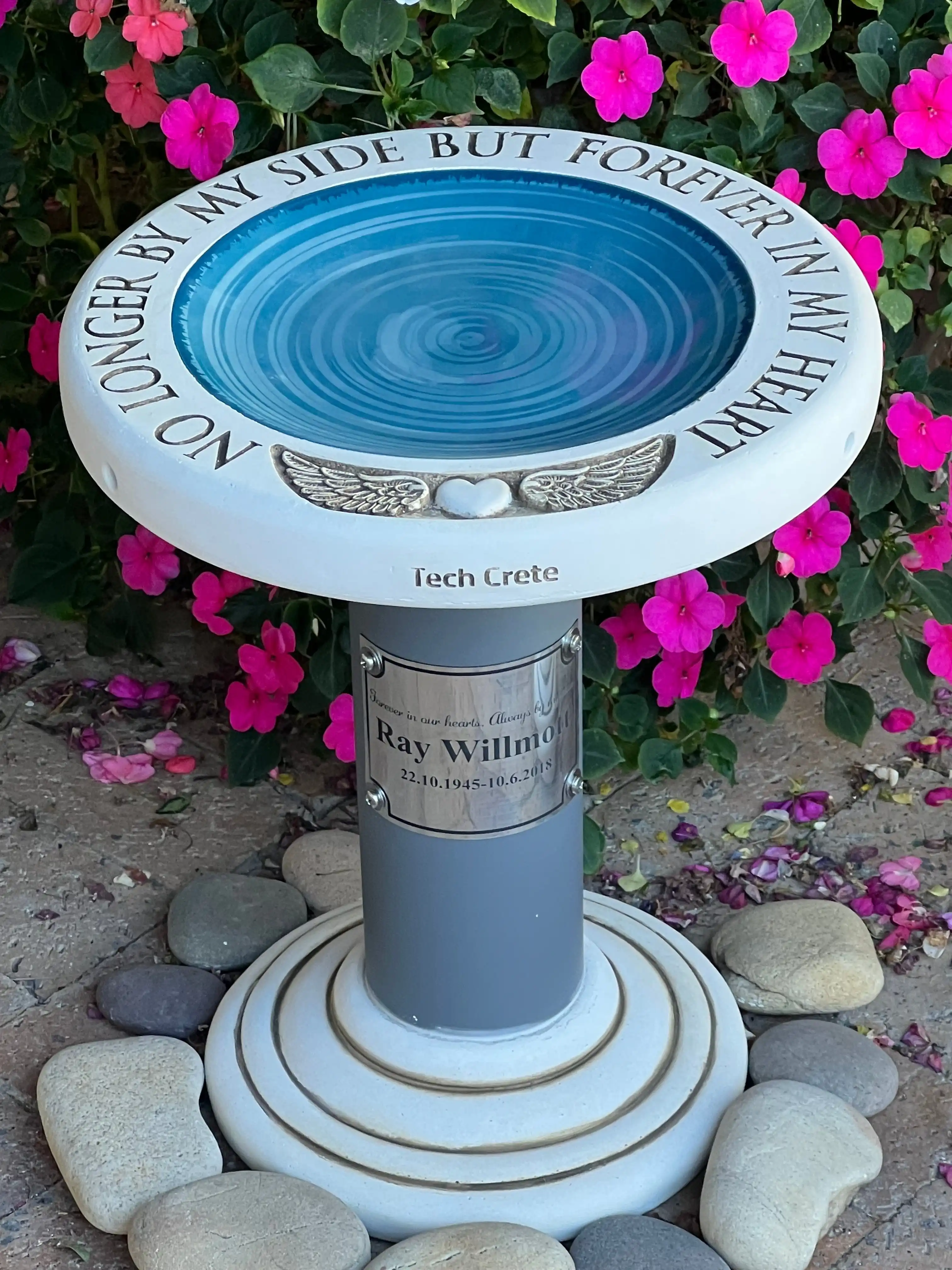 Handcrafted concrete memorial birdbath engraved with a tribute, set among flowers